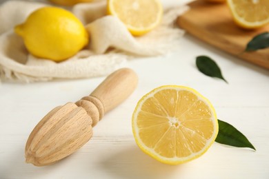 Photo of Wooden citrus reamer and halved fresh lemon on white table, closeup
