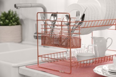 Photo of Drying rack with clean dishes and cutlery on countertop near sink in kitchen