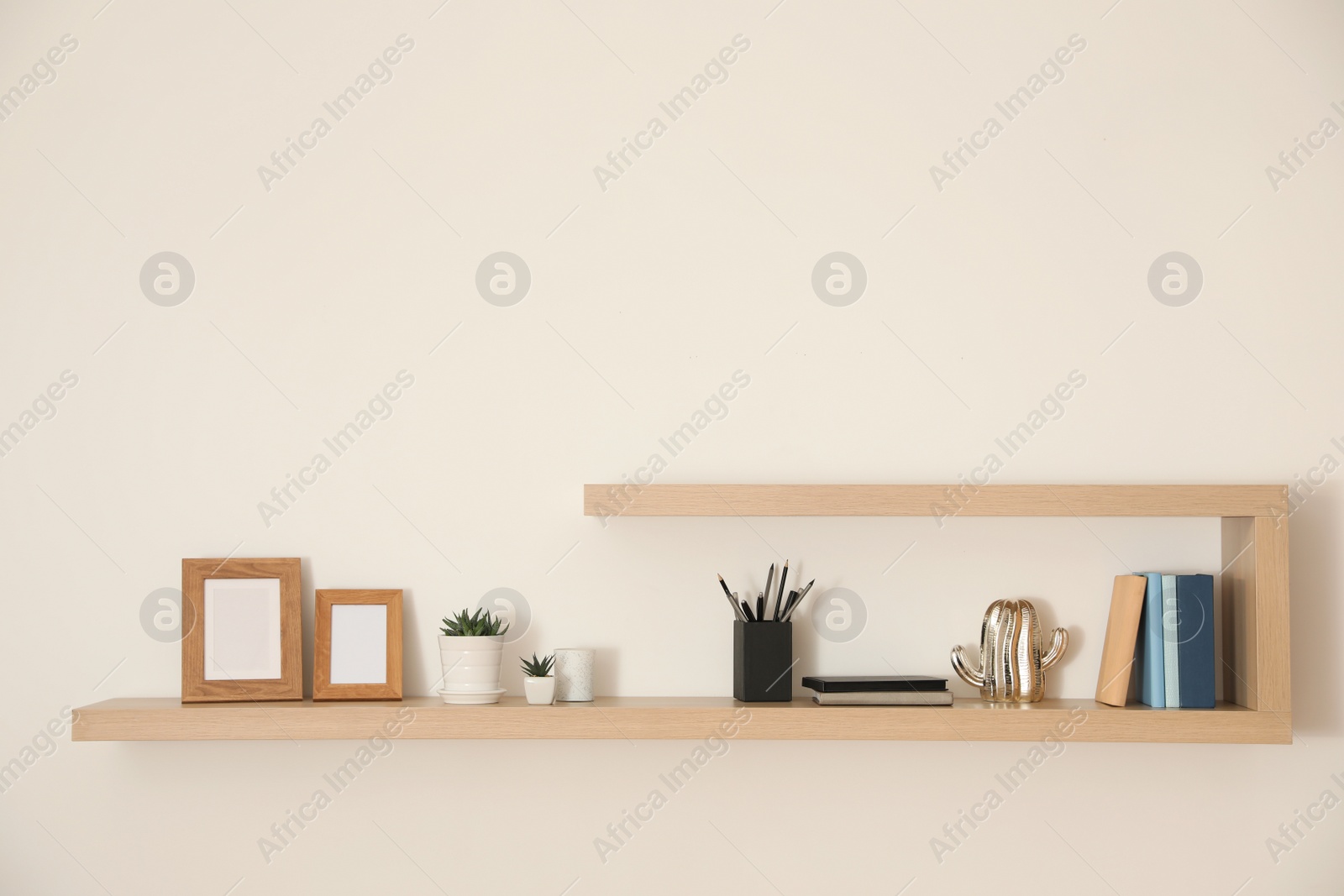 Photo of Wooden shelves with books, photo frames and decorative elements on light wall