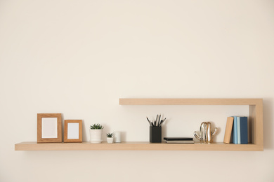 Photo of Wooden shelves with books, photo frames and decorative elements on light wall