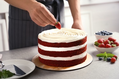 Photo of Woman decorating delicious homemade red velvet cake with strawberry at table