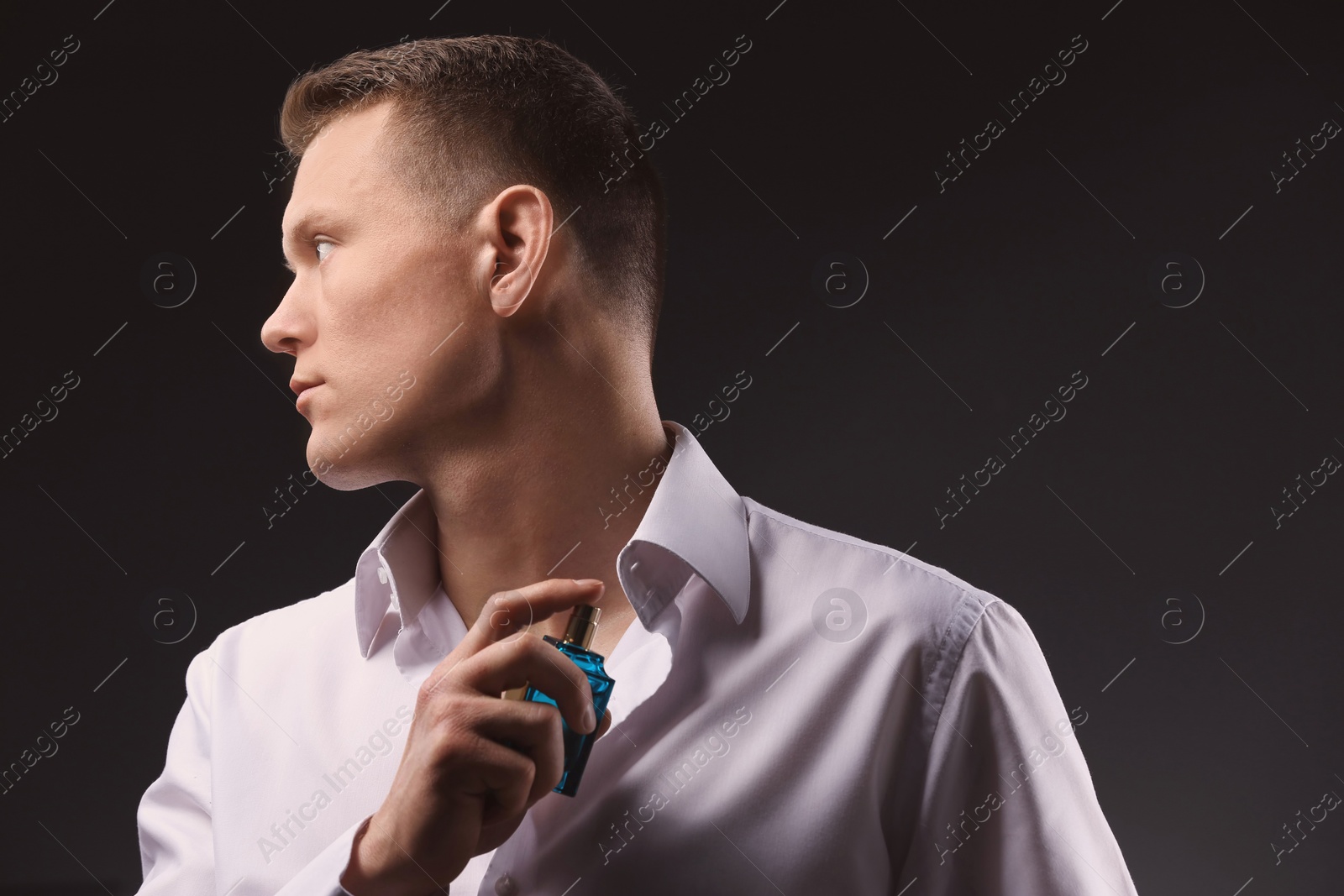 Photo of Handsome man in shirt using perfume on dark background