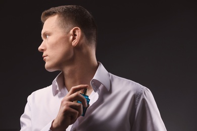 Photo of Handsome man in shirt using perfume on dark background