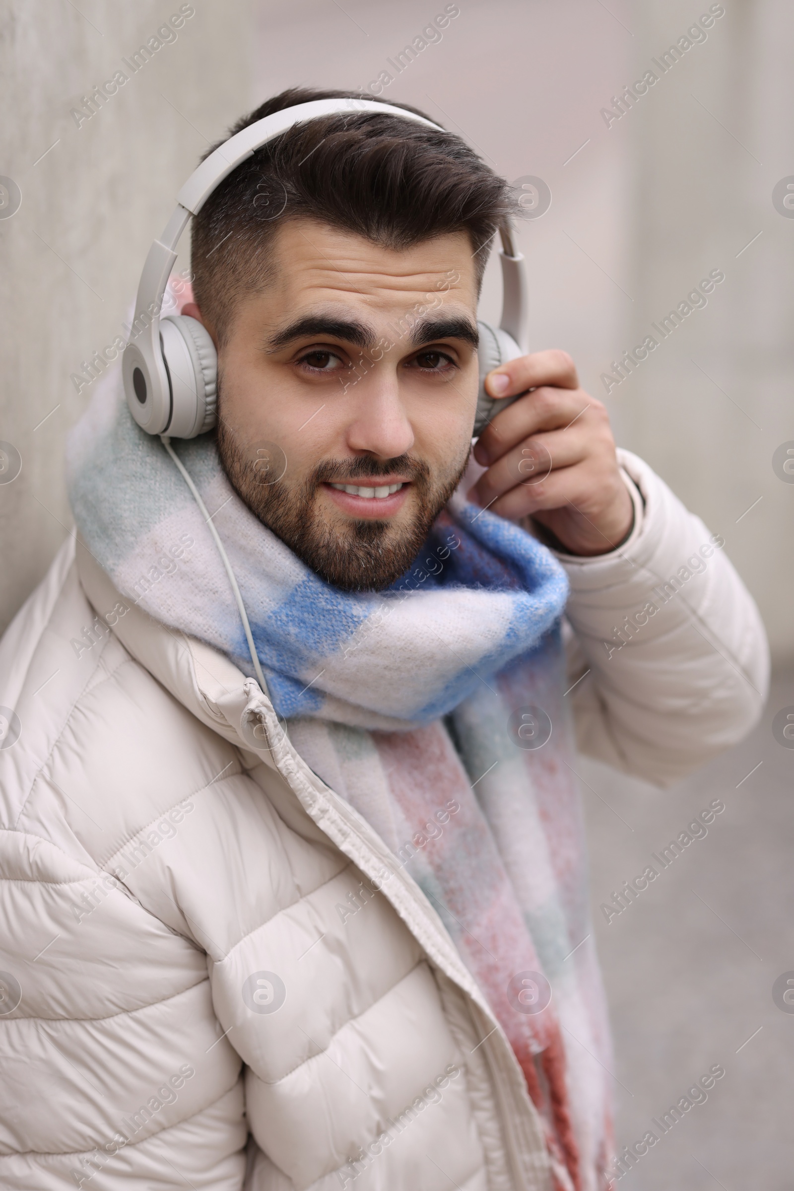 Photo of Smiling man in warm scarf and headphones on blurred background