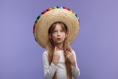 Photo of Cute girl in Mexican sombrero hat pointing at something on purple background