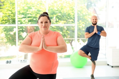 Photo of Overweight man and woman practicing yoga in gym