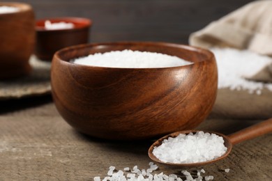 Photo of Bowl and spoon with natural sea salt on wooden table, closeup