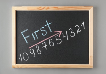 Chalkboard with word FIRST and numbers on grey background, top view. Victory concept