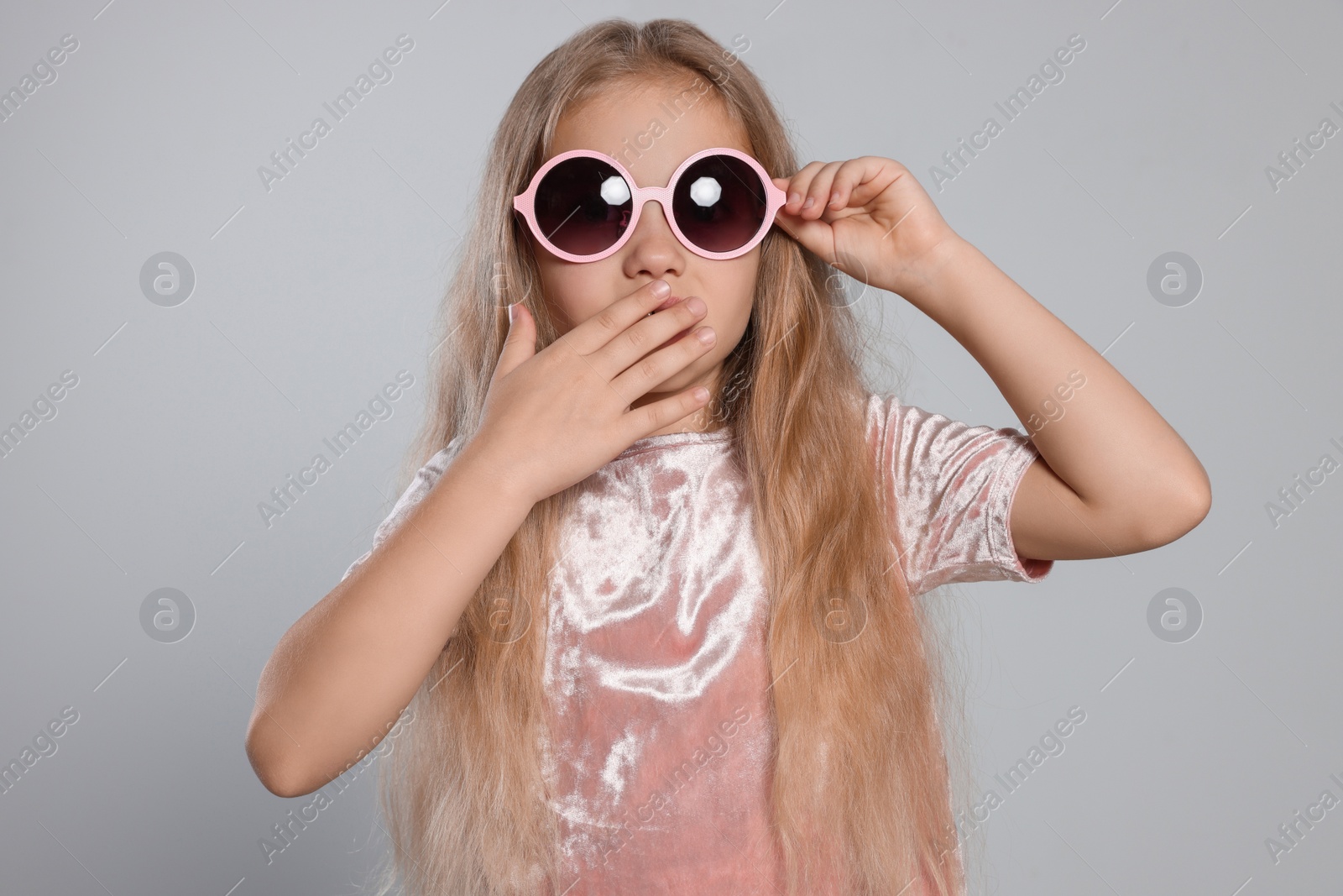 Photo of Girl in stylish sunglasses covering mouth with hand on light grey background