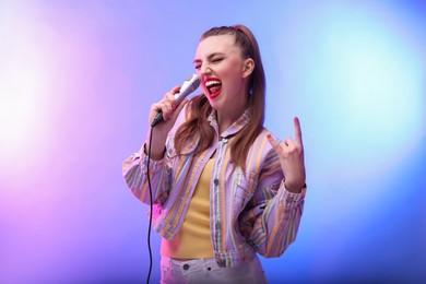 Emotional woman with microphone singing and showing rock gesture in color lights