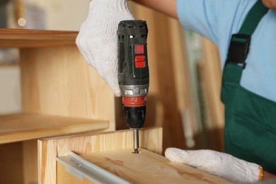 Professional carpenter twisting screw into wooden drawer in workshop, closeup