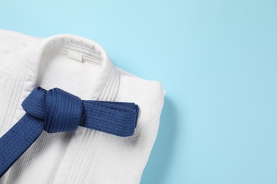 Photo of Karate belt and white kimono on light blue background, top view. Space for text