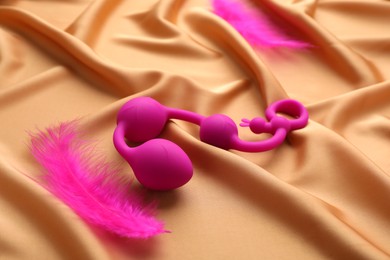 Photo of Pink anal balls and feathers on golden silk fabric. Sex toy