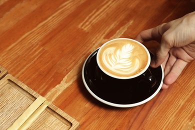 Photo of Barista putting cup of coffee on wooden table, closeup. Space for text