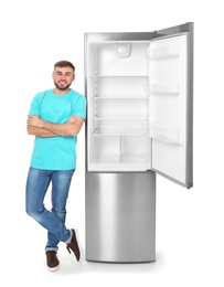 Young man near empty refrigerator on white background