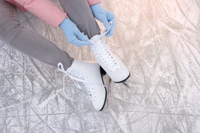 Woman lacing figure skates on ice, top view