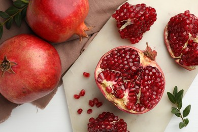 Photo of Fresh pomegranates and branches on white table, flat lay