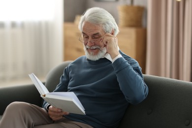 Portrait of happy grandpa reading book on sofa indoors
