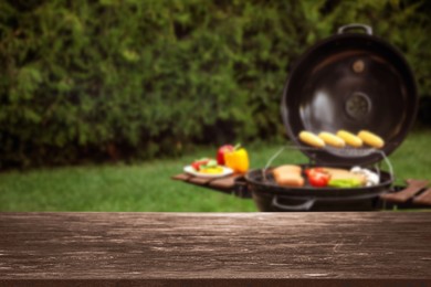 Empty wooden table and blurred view of tasty food on modern barbecue grill outdoors