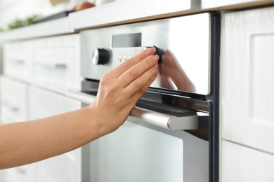 Photo of Woman regulating cooking mode on oven panel in kitchen, closeup