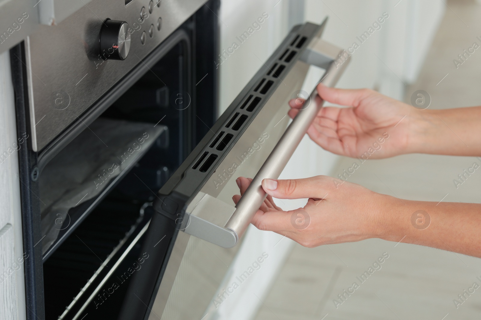 Photo of Young woman opening electric oven in kitchen, closeup