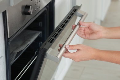 Young woman opening electric oven in kitchen, closeup