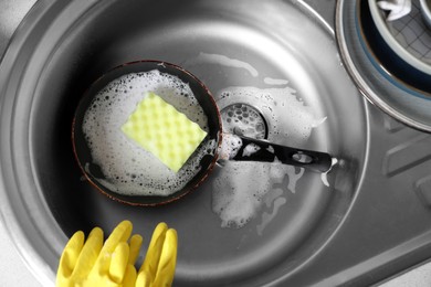 Photo of Dirty frying pan with sponge in kitchen sink, above view