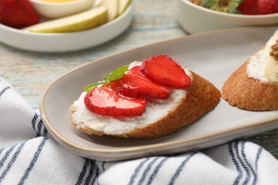Photo of Delicious ricotta bruschettas with strawberry and mint on wooden table, closeup