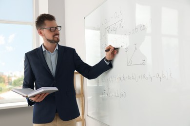 Photo of Happy teacher with book explaining mathematics at whiteboard in classroom
