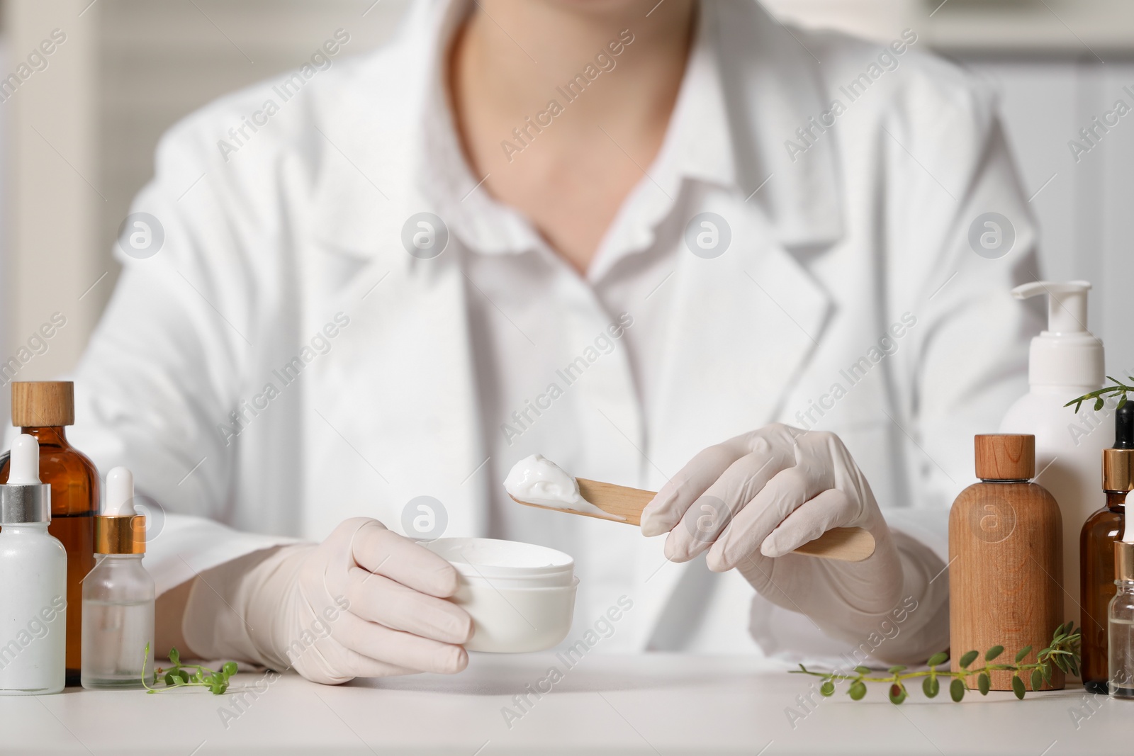 Photo of Dermatologist with jar testing cosmetic product at white table indoors, selective focus