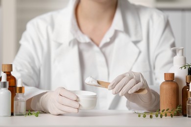 Dermatologist with jar testing cosmetic product at white table indoors, selective focus