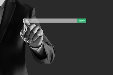 Businessman using search bar of website on virtual screen, closeup. Black and white photo
