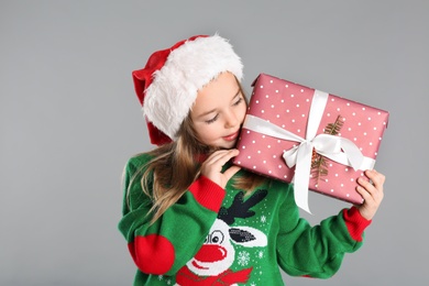 Photo of Cute child in Santa hat with Christmas gift on grey background