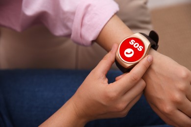 Woman using SOS function on smartwatch indoors, closeup