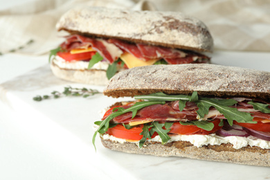 Delicious sandwiches with fresh vegetables and prosciutto on white table, closeup