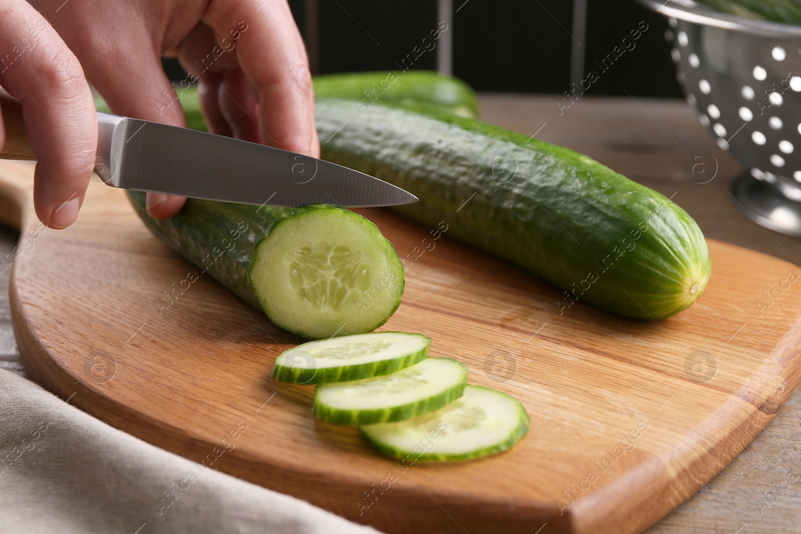 Photo of Woman cutting cucumber on wooden board at table, closeup