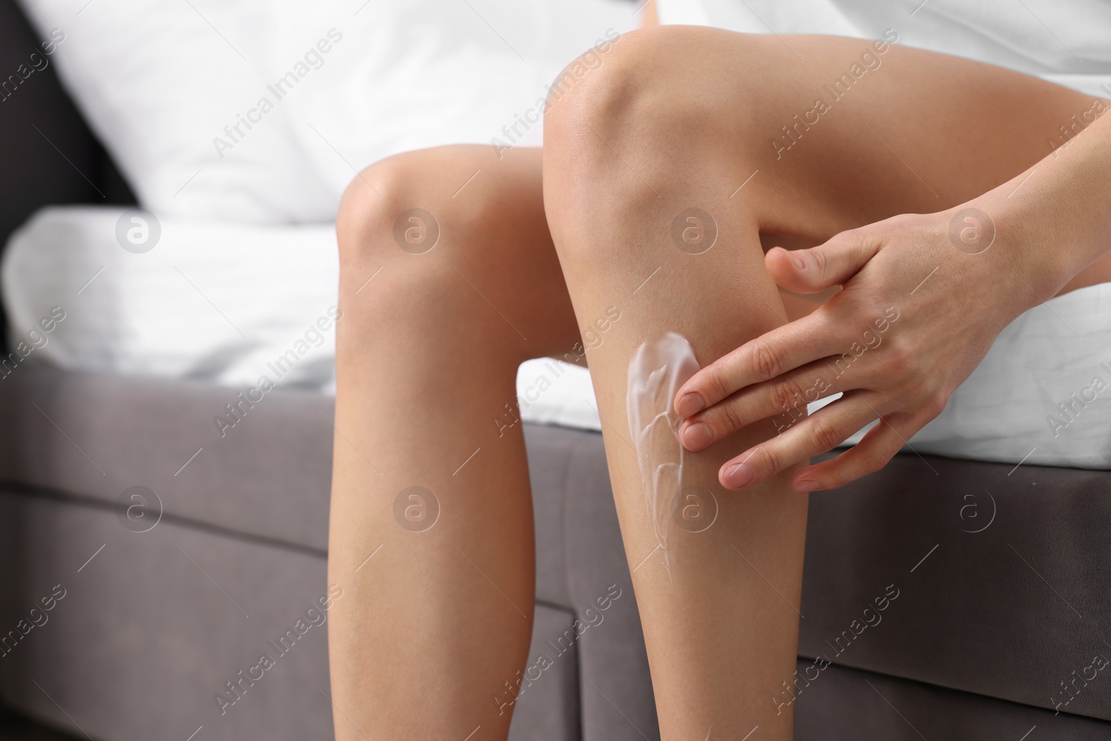 Photo of Woman applying cream onto leg in bedroom, closeup