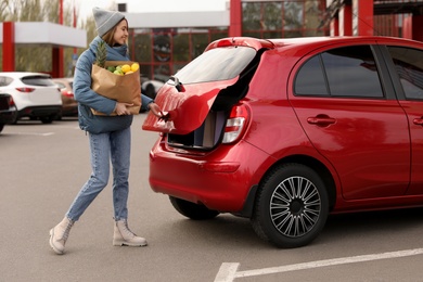 Photo of Young woman with bag of groceries near her car outdoors