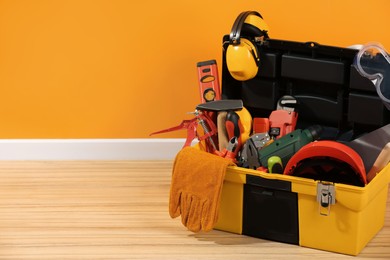 Box with different tools for repair on floor near orange wall, space for text