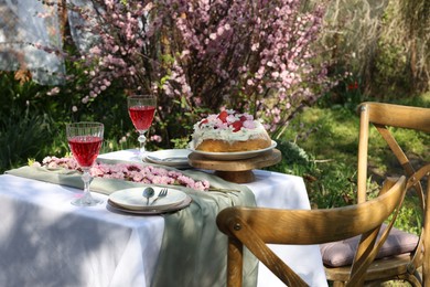 Photo of Beautiful spring flowers, delicious cake and wine glasses on table in garden