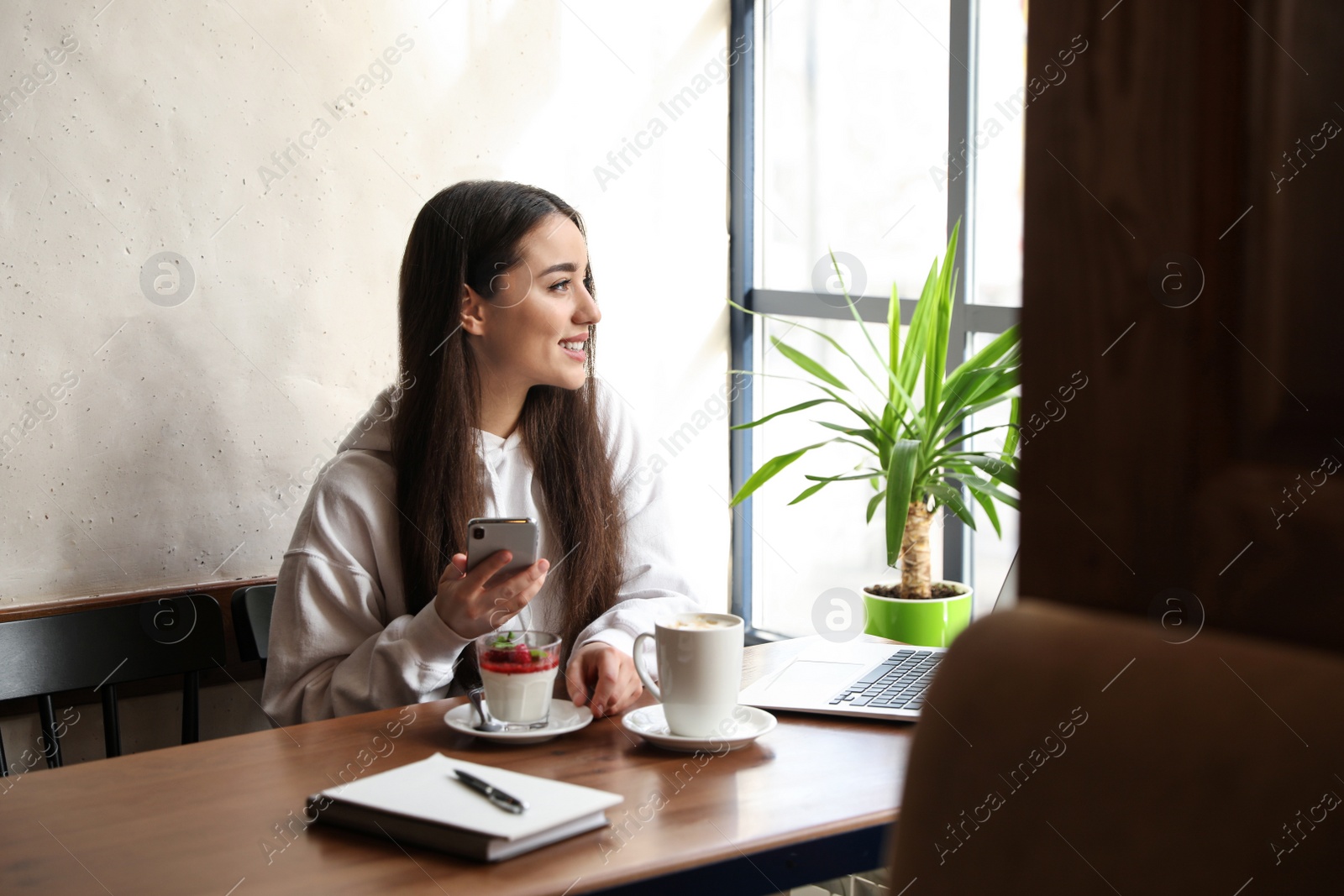 Photo of Young blogger with phone at table in cafe