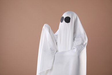Photo of Creepy ghost. Person covered with white sheet on dark beige background, space for text