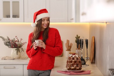 Photo of Beautiful young woman in Santa hat with cup of tea in kitchen. Celebrating Christmas
