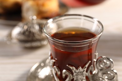 Photo of Glass of traditional Turkish tea in vintage holder on table, closeup