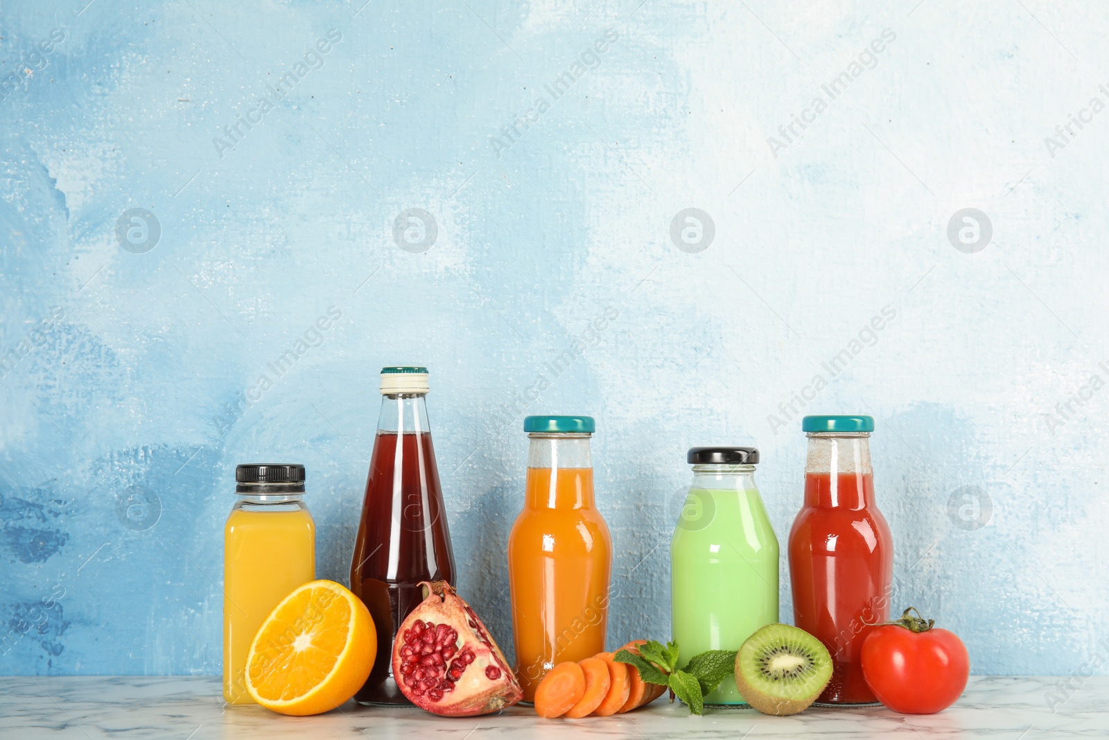 Photo of Bottles with different drinks and ingredients on table against color background