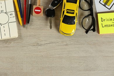 Photo of Flat lay composition with driving lessons workbook and toy car on wooden background, space for text. Passing license exam