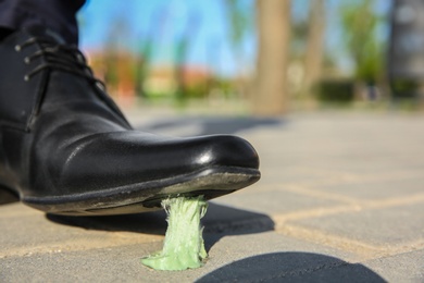 Photo of Man stepping in chewing gum on sidewalk. Concept of stickiness