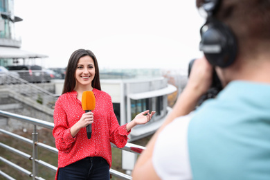 Young journalist and video operator working on city street