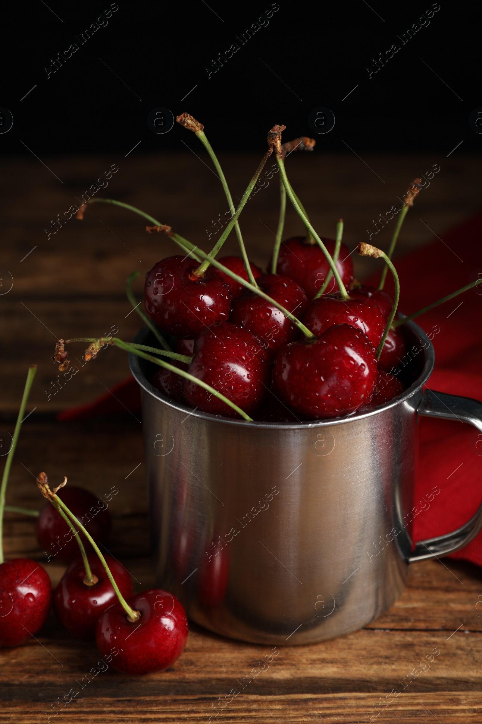 Photo of Wet red cherries in enameled mug on wooden table