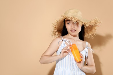 Photo of Beautiful young woman in straw hat holding sun protection cream on beige background, space for text